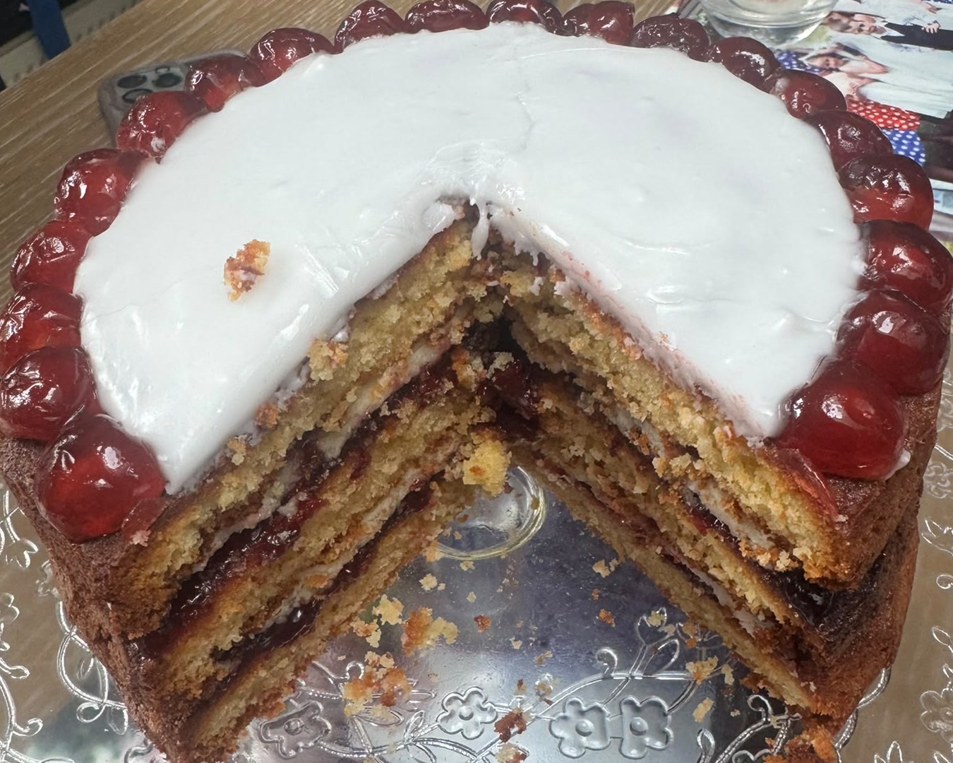 The same cake with a large slice cut out, showing layers of almond sponge with dark cherry compote between them. The same cake with a large slice cut out, showing layers of almond sponge with dark cherry compote between them.