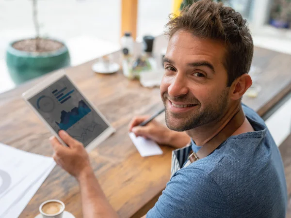 Man smiling at desk while reviewing data on tablet, symbolising creating helpful content for business visibility in AI Overviews.