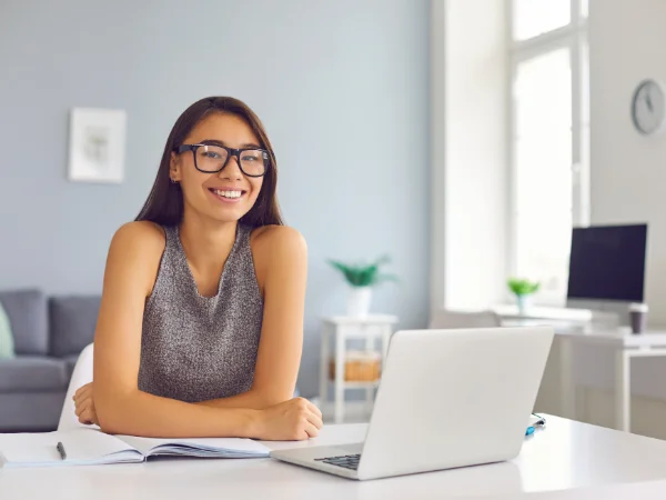 Smiling woman with glasses working on laptop at home, symbolising small business owners building authority and online presence.