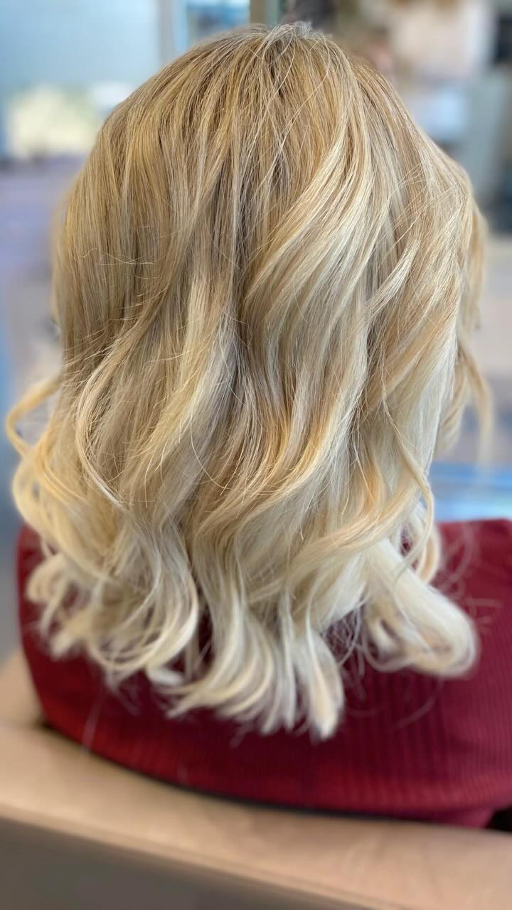 Lange blonde Haare mit hellem Balayage-Verlauf, dunklerem Ansatz und weichen Wellen