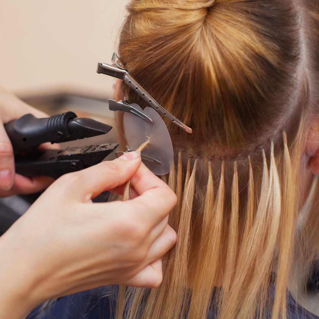 Friseurin hält Echthaarsträhnen zum Farbvergleich an das Naturhaar einer Kundin im Beratungsgespräch