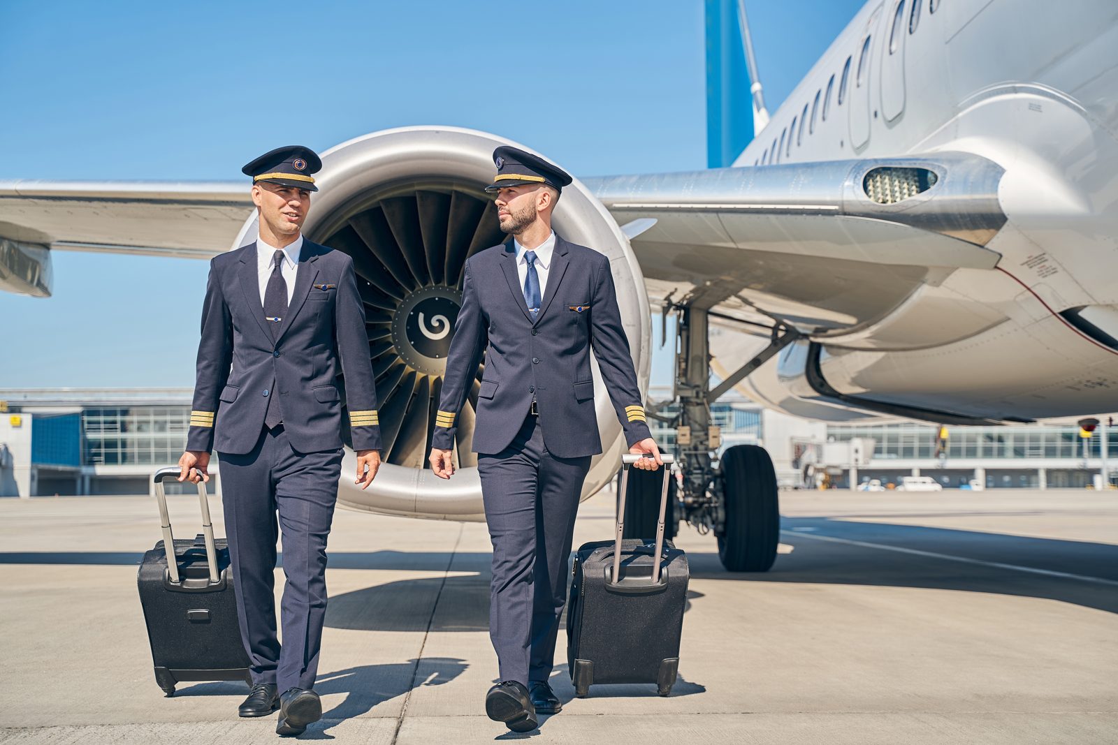 Two pilots in uniform walking across the apron past an airliner