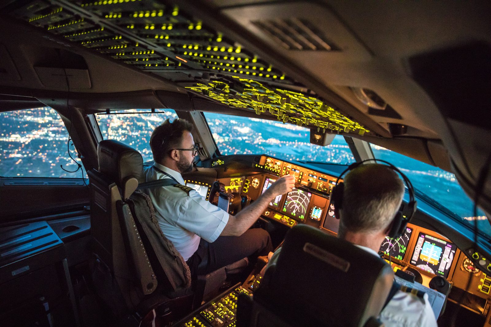 Two pilots at the controls on the flight deck of an airliner at dusk