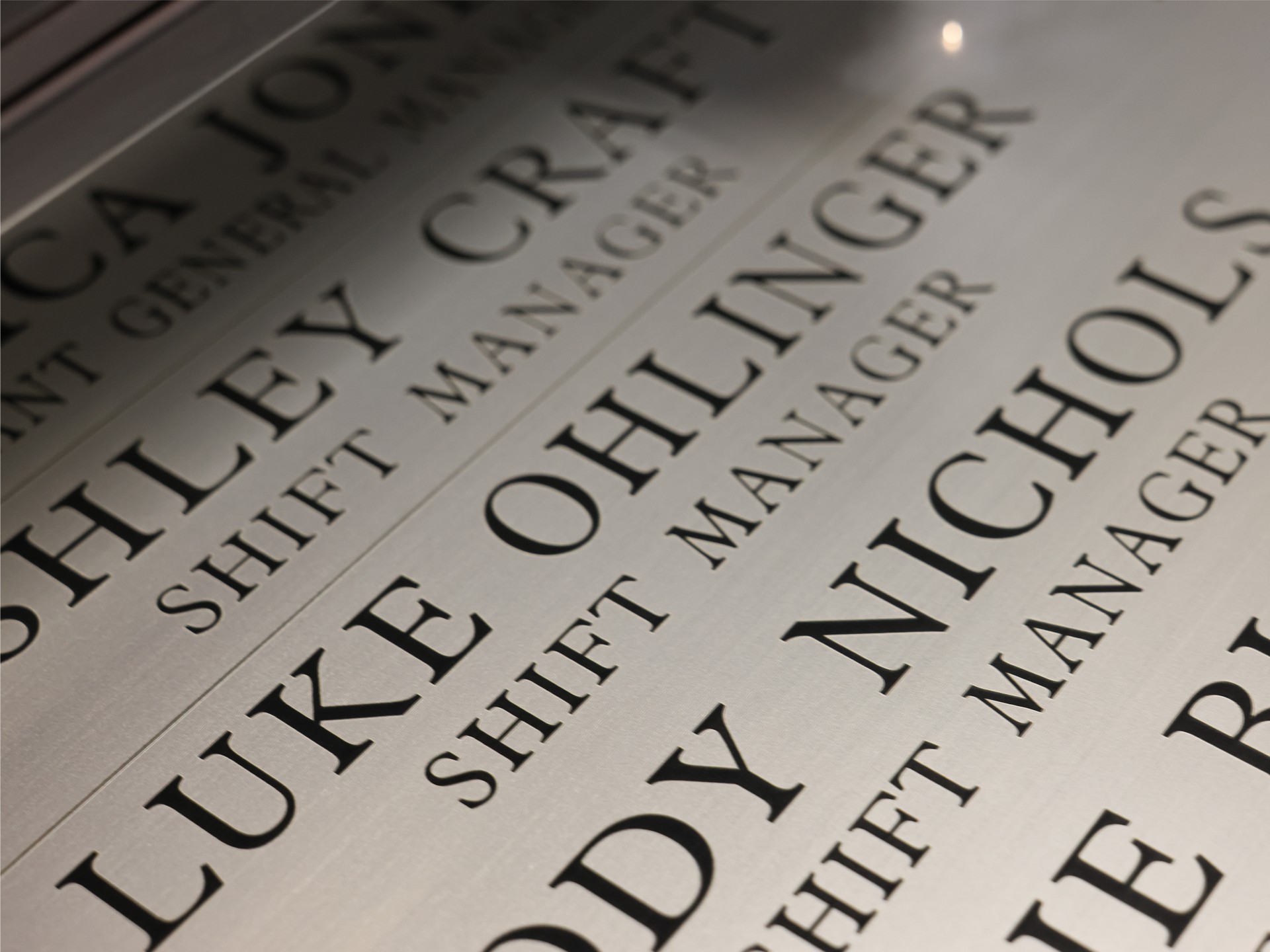 Engraved brushed stainless nameplate board listing names and job titles, shot at a raking angle
