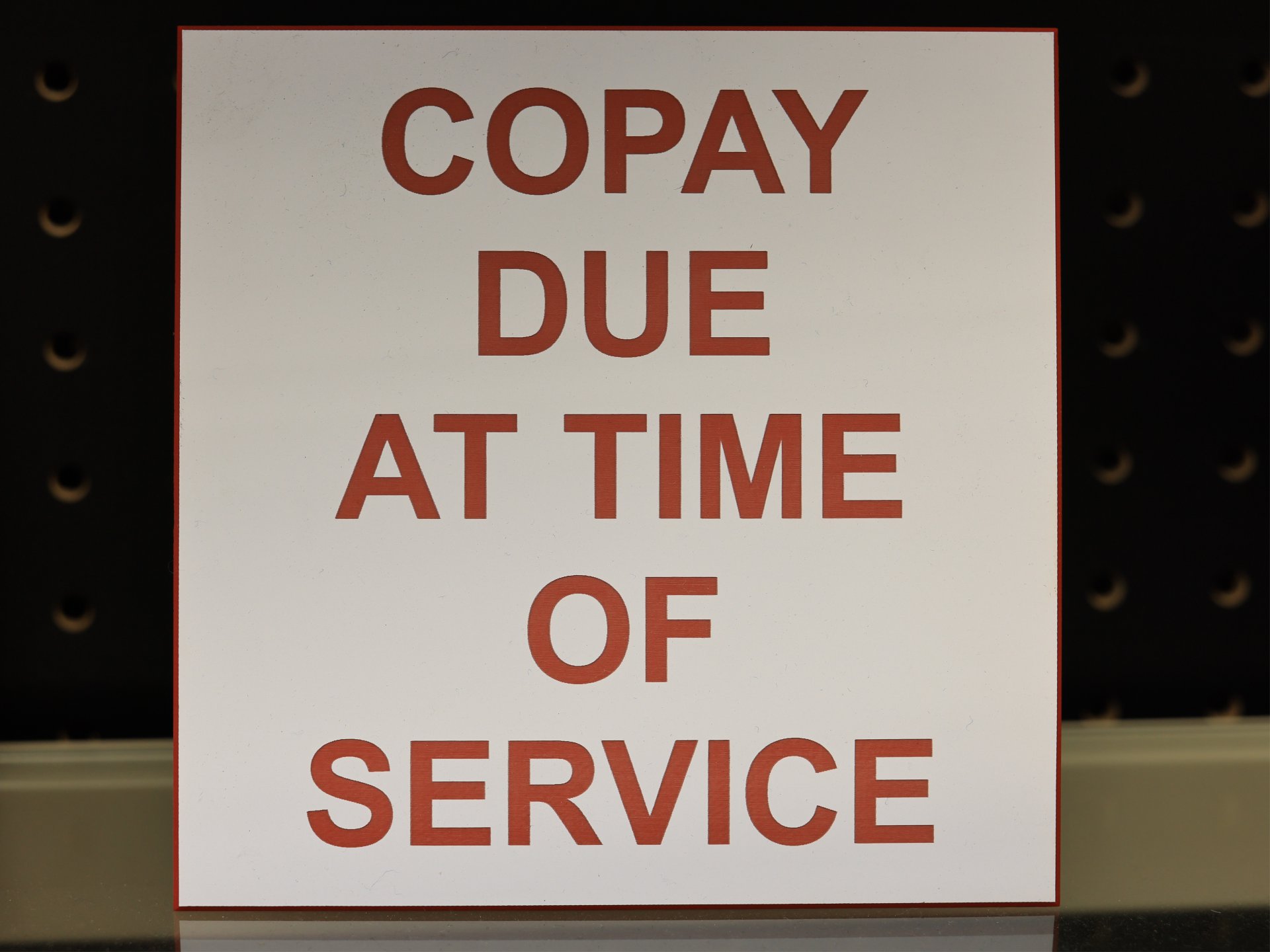 Engraved white and red placard reading Copay Due At Time Of Service, with the red core showing at the bevelled edge