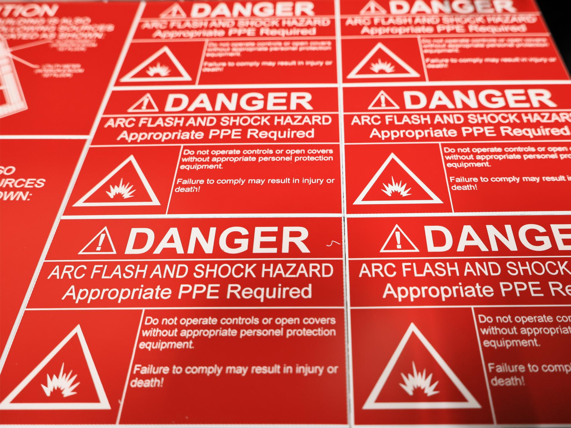 Engraved red arc flash danger labels reading Arc Flash and Shock Hazard, Appropriate PPE Required, in a production run