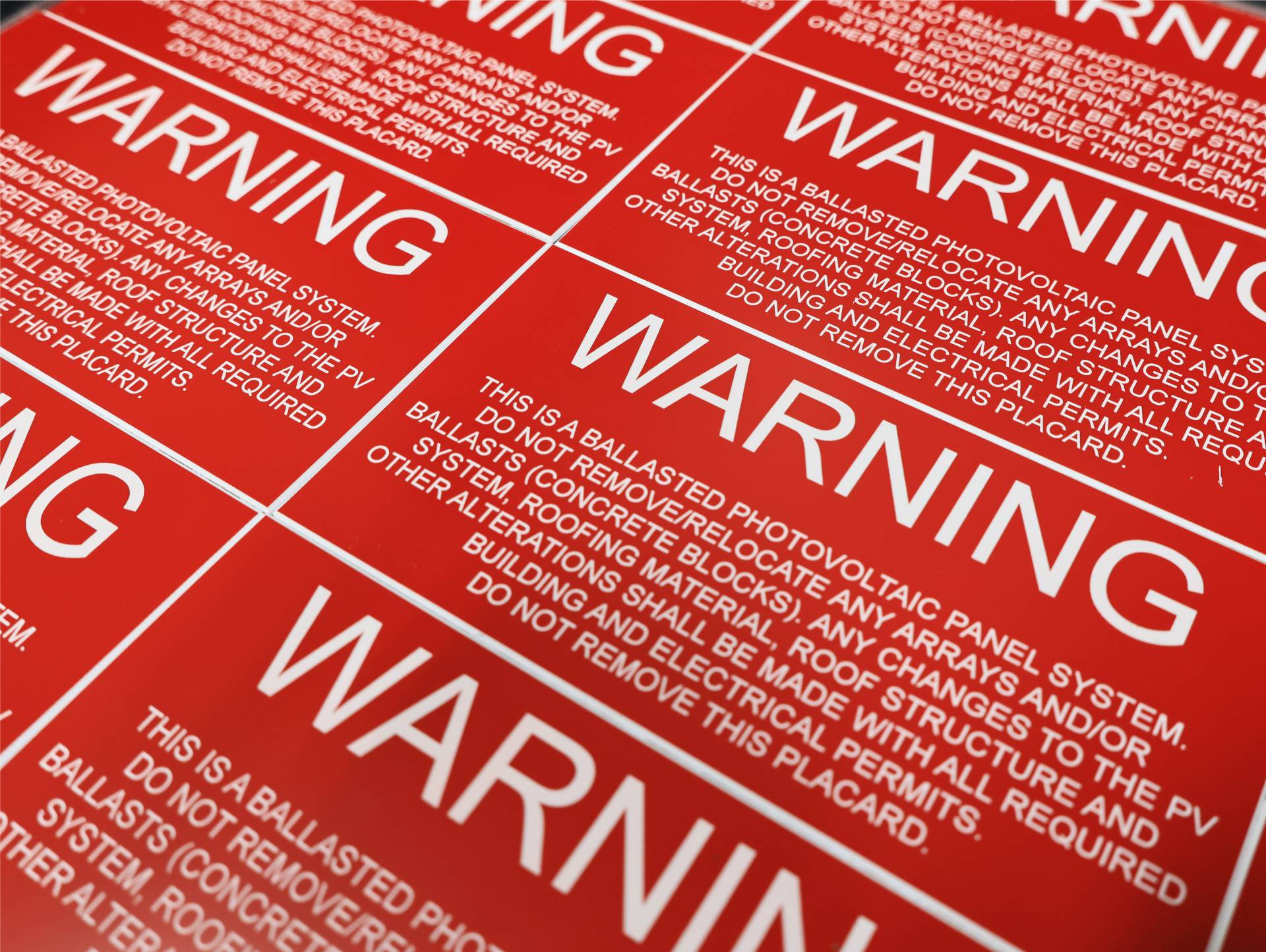 Engraved red warning placards for a ballasted photovoltaic panel system, repeating across a production sheet