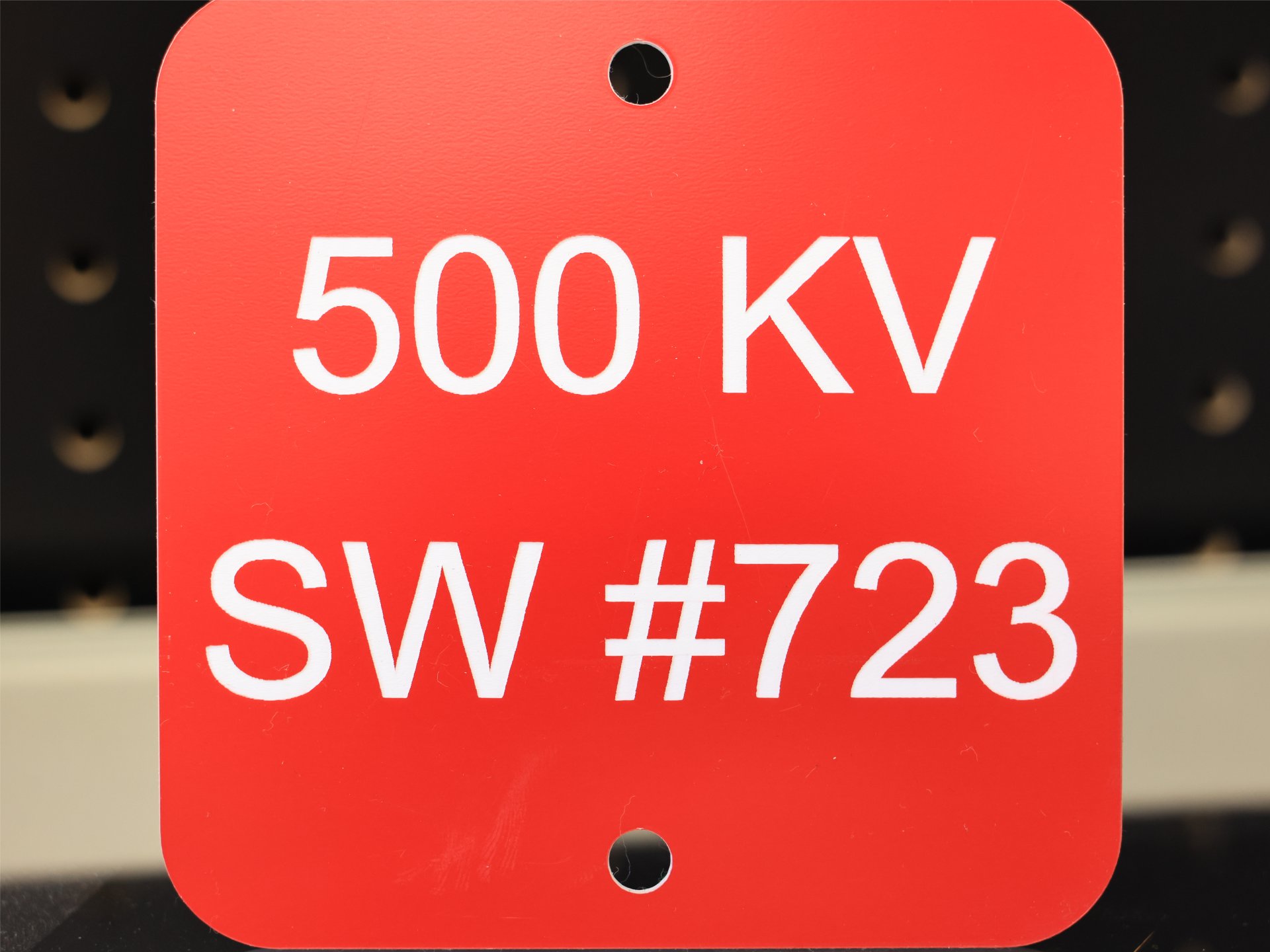 Engraved red phenolic substation switch tag reading 500 KV SW #723, with mounting holes top and bottom