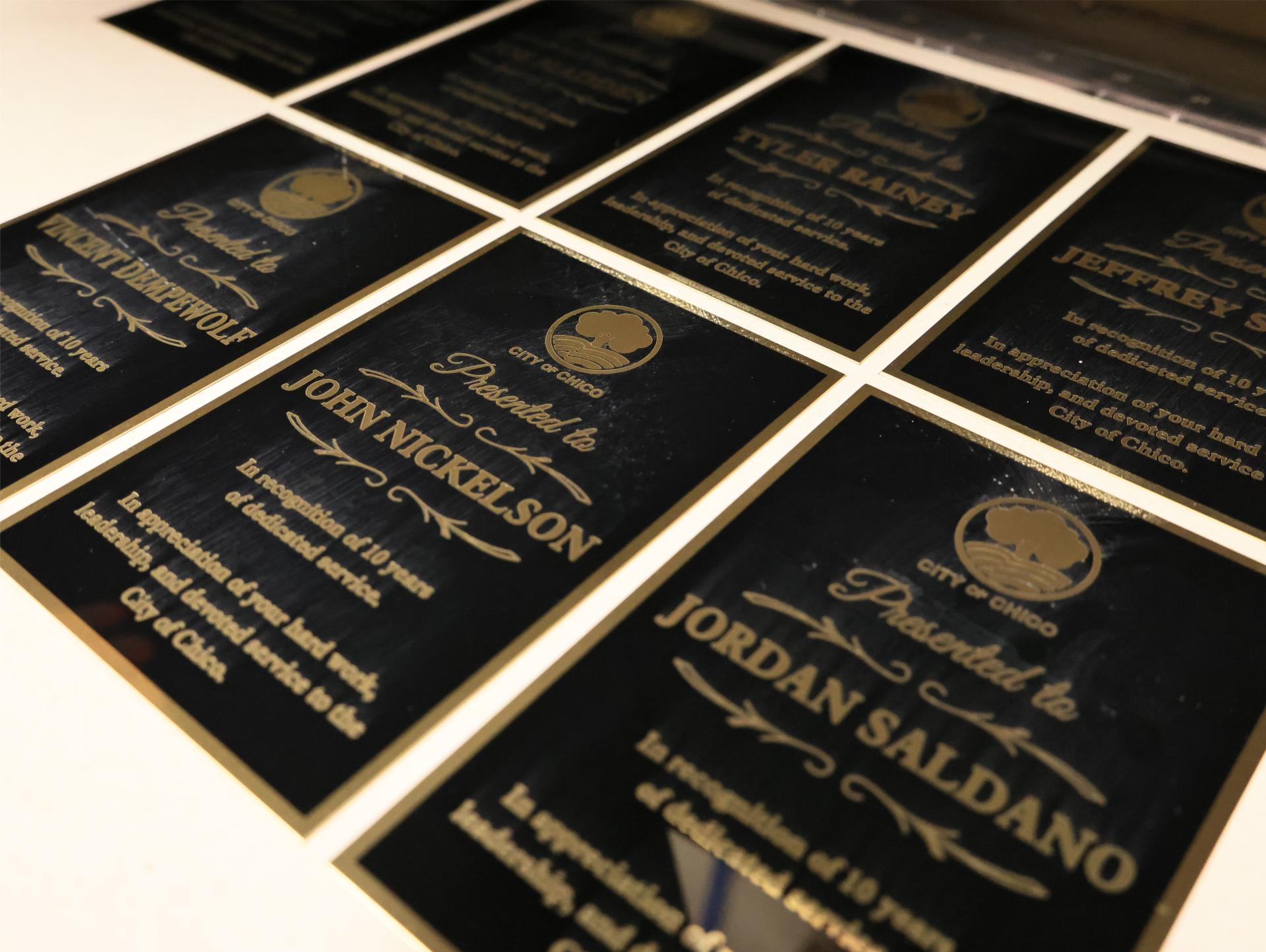 Black and gold engraved service award plates carrying a city seal, arranged in rows