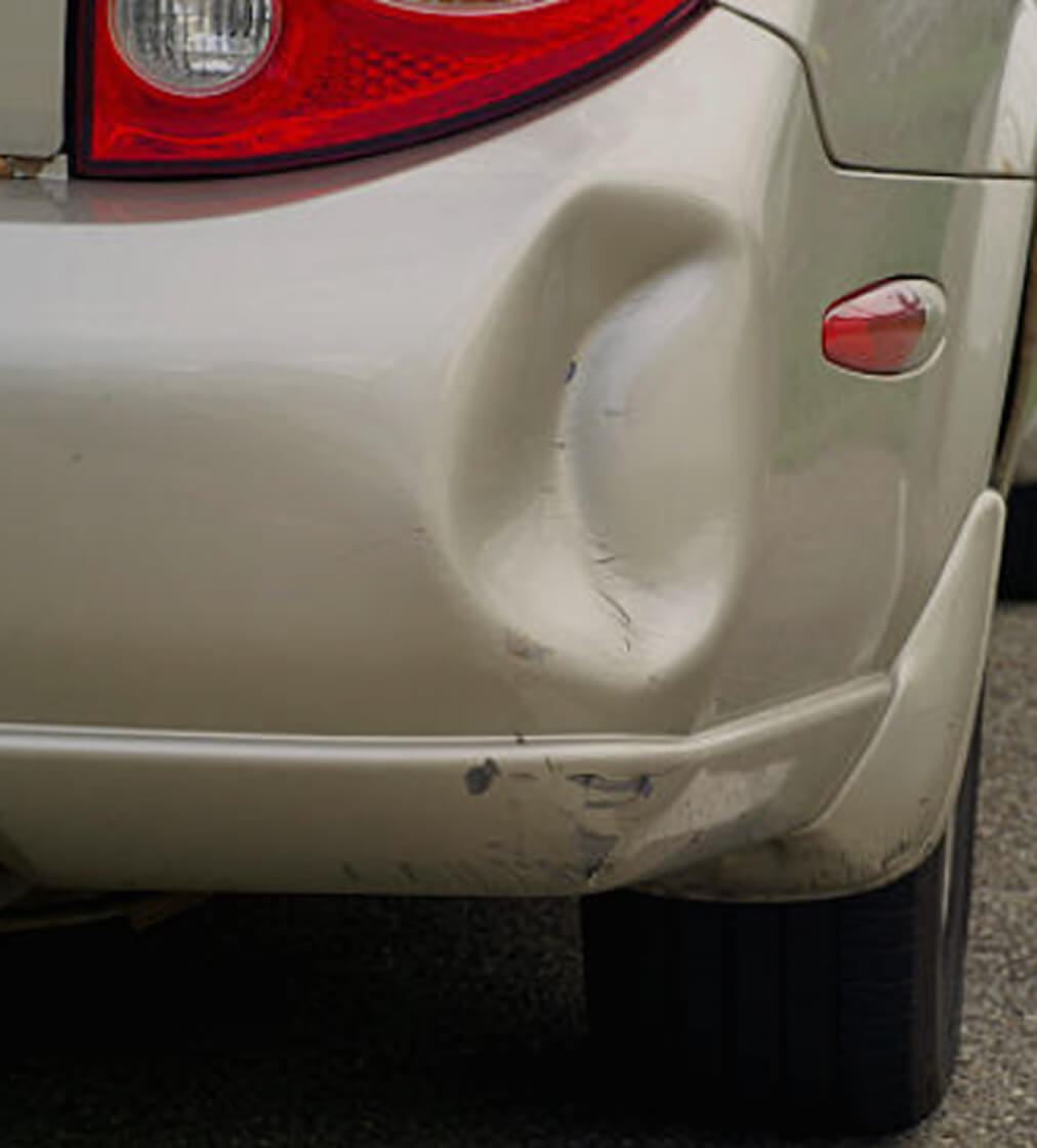 Rear bumper cover of a silver car creased and scuffed by a low-speed impact, with the body panel above it undamaged