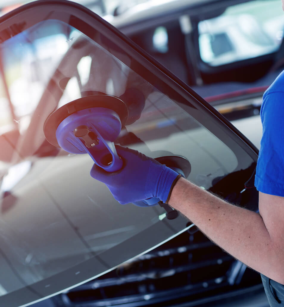 Technician in gloves setting a new windshield into a vehicle using suction cup handles