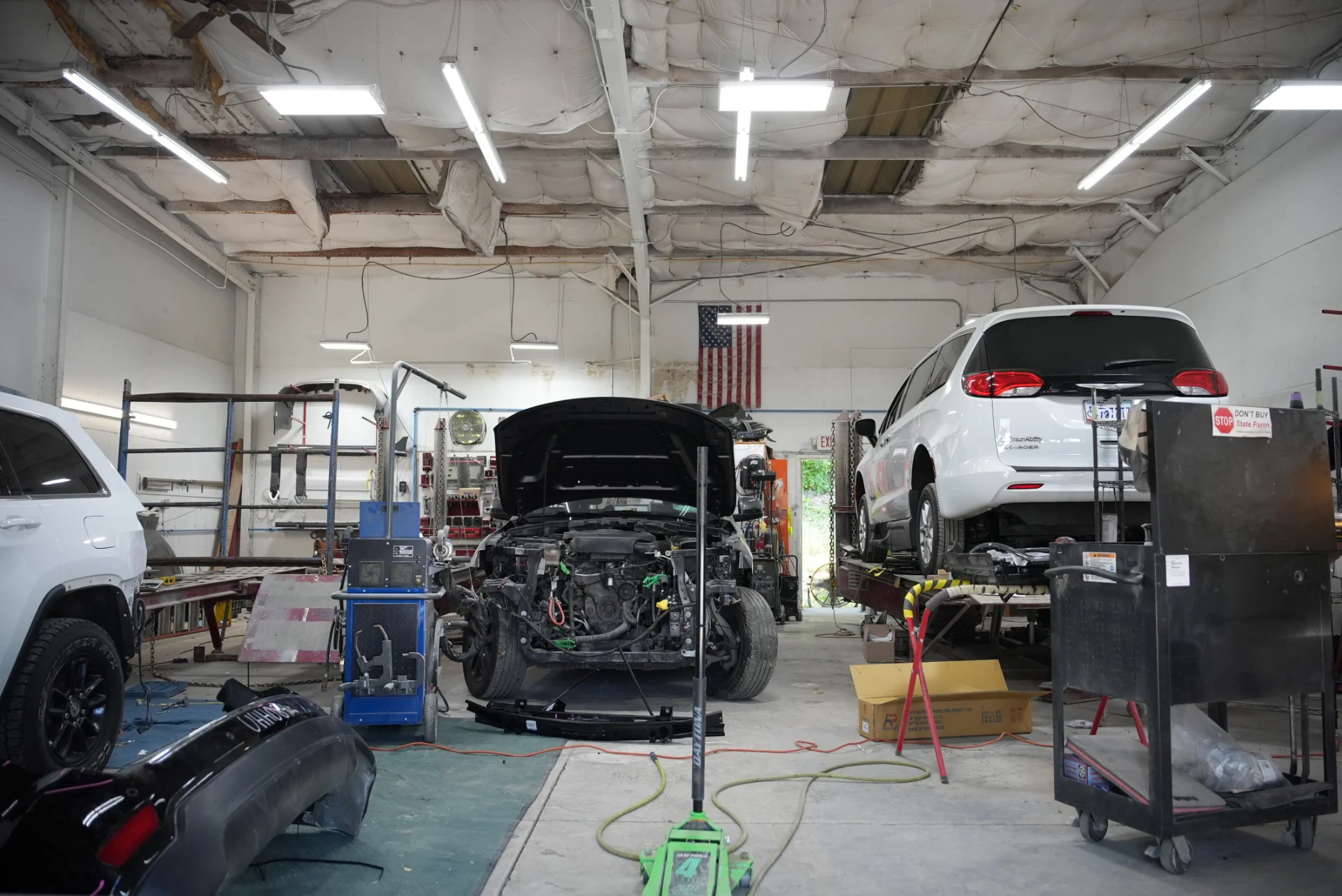 Inside the Excite Collision Repair shop, a vehicle on a frame rack mid-repair and another up on a lift