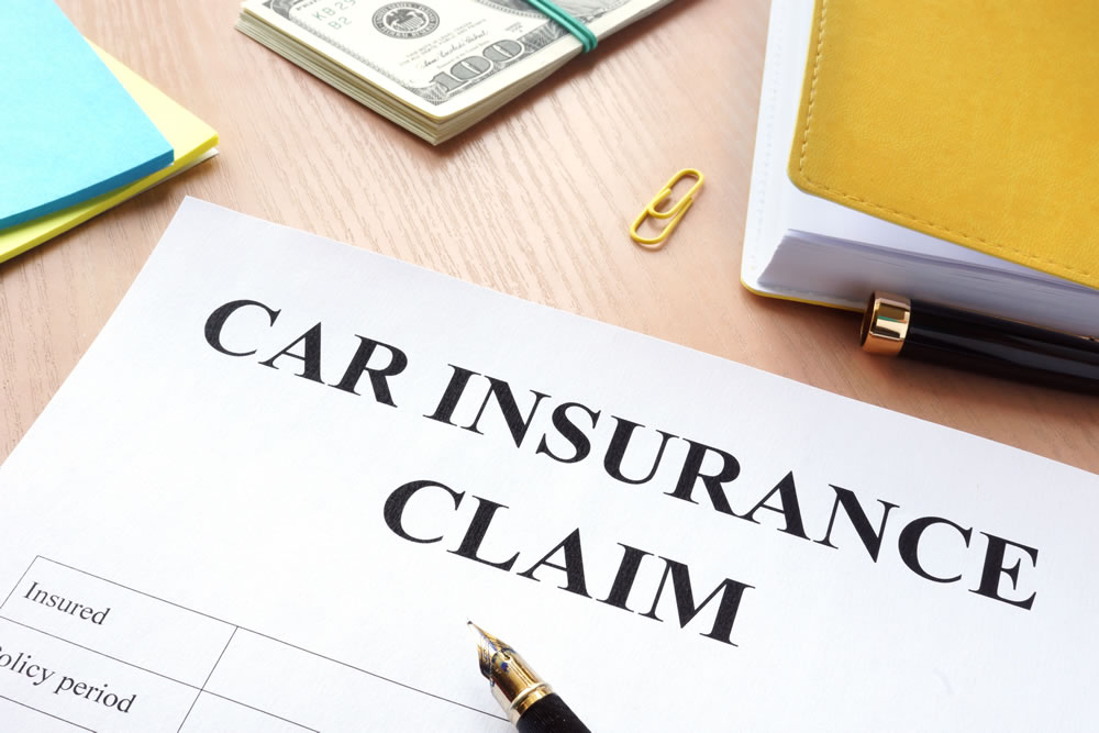 A printed car insurance claim form on a desk with a pen, cash and a folder