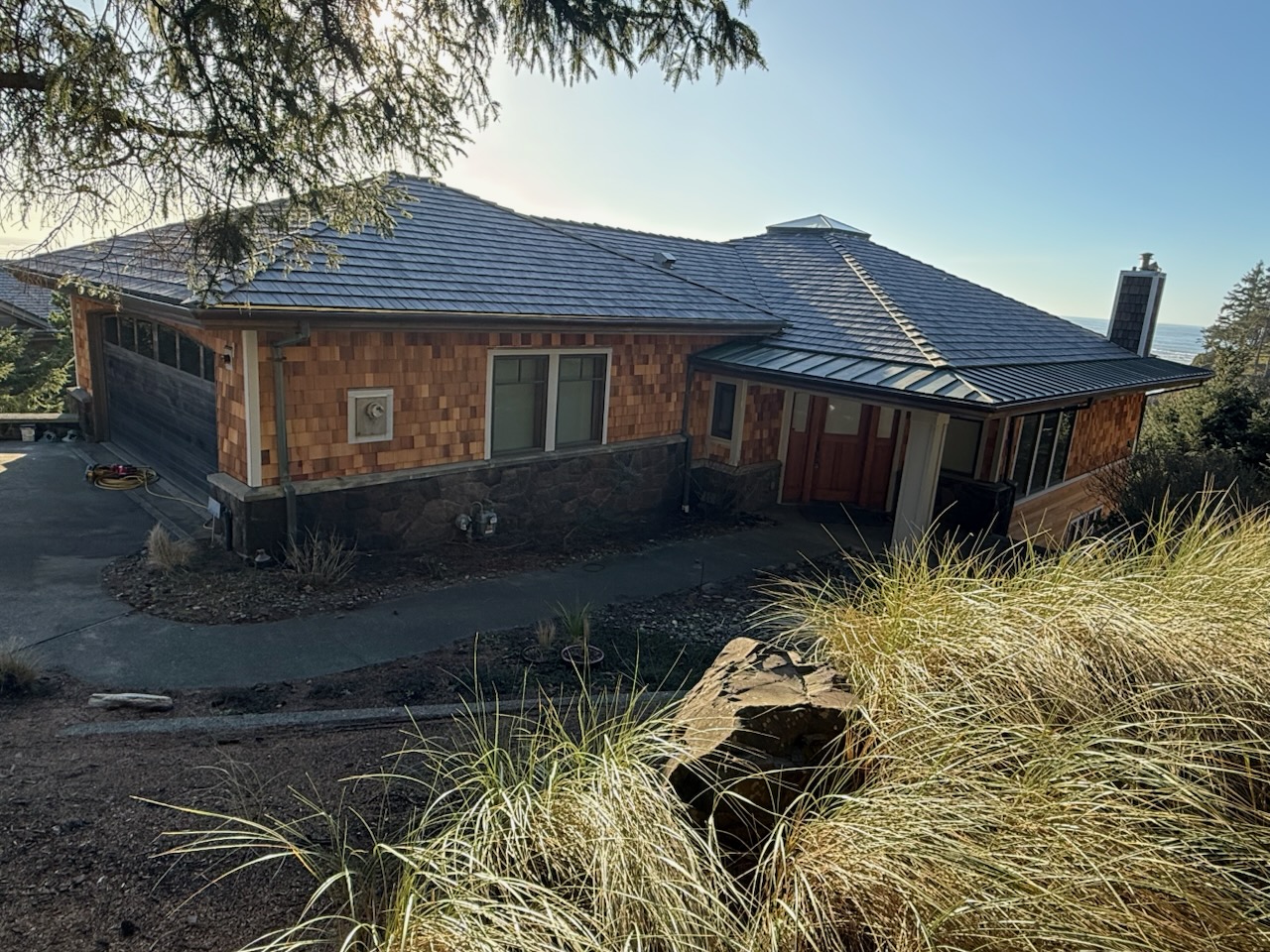 Cannon Beach home after complete exterior renovation with new synthetic slate roof, fresh cedar shake siding, and stone veneer