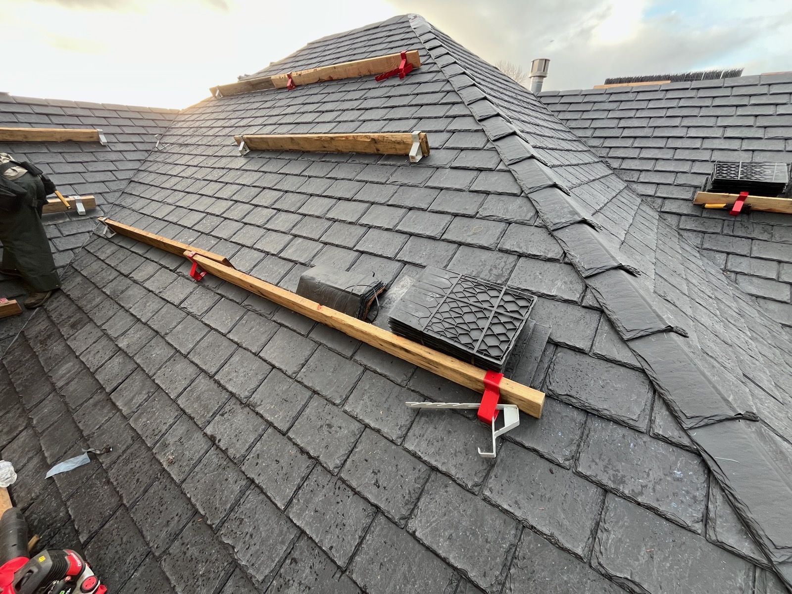 Synthetic slate roof installation showing premium composite slate tiles, hip caps, and roof jacks staged for crew