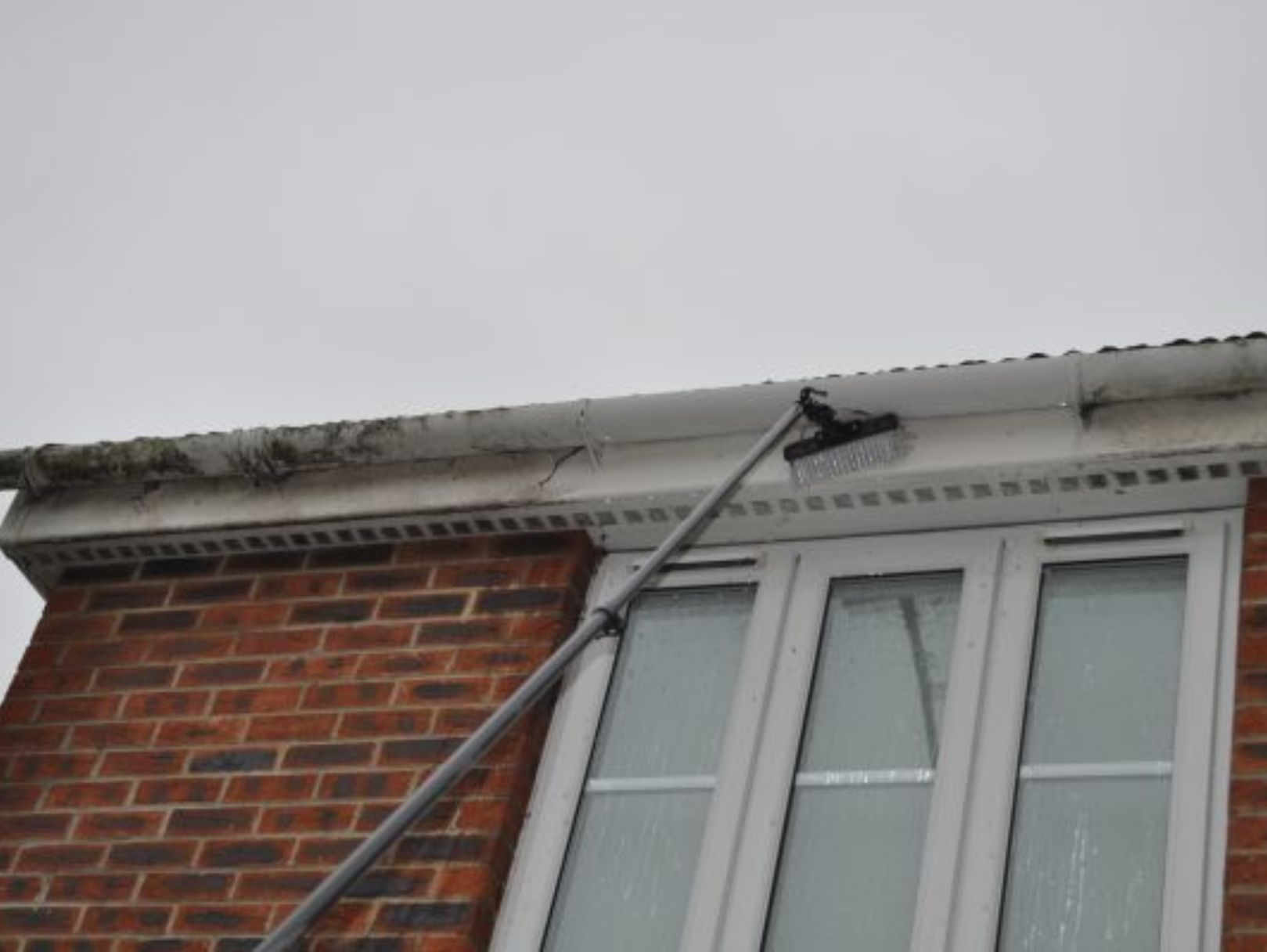 Water-fed pole cleaning fascias and gutters on a brick house