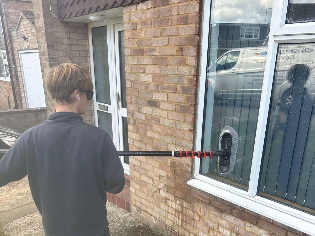 A Clear View team member cleaning a ground floor window with a water fed pole, seen from behind
