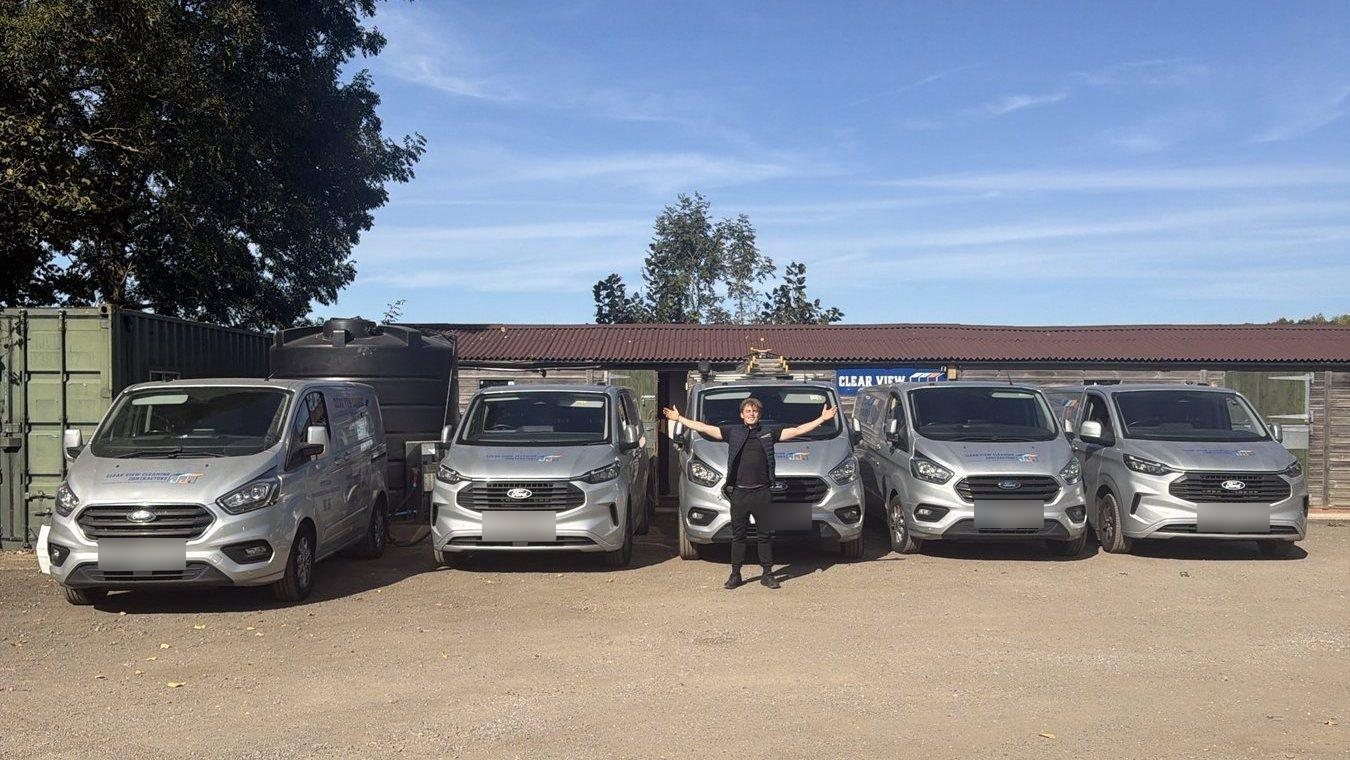 Dylan with his arms out in front of five Clear View vans at our base in Colney Heath