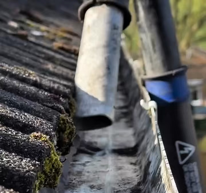 A gutter packed with moss being vacuumed clear, with water running along the cleared gutter