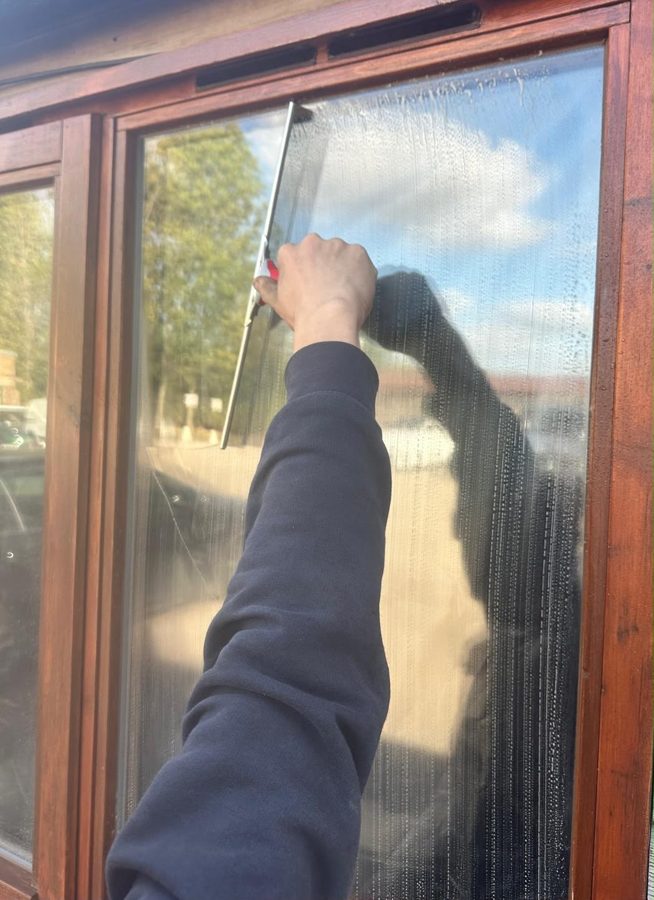 A Clear View window cleaner squeegeeing a wooden-framed window by hand