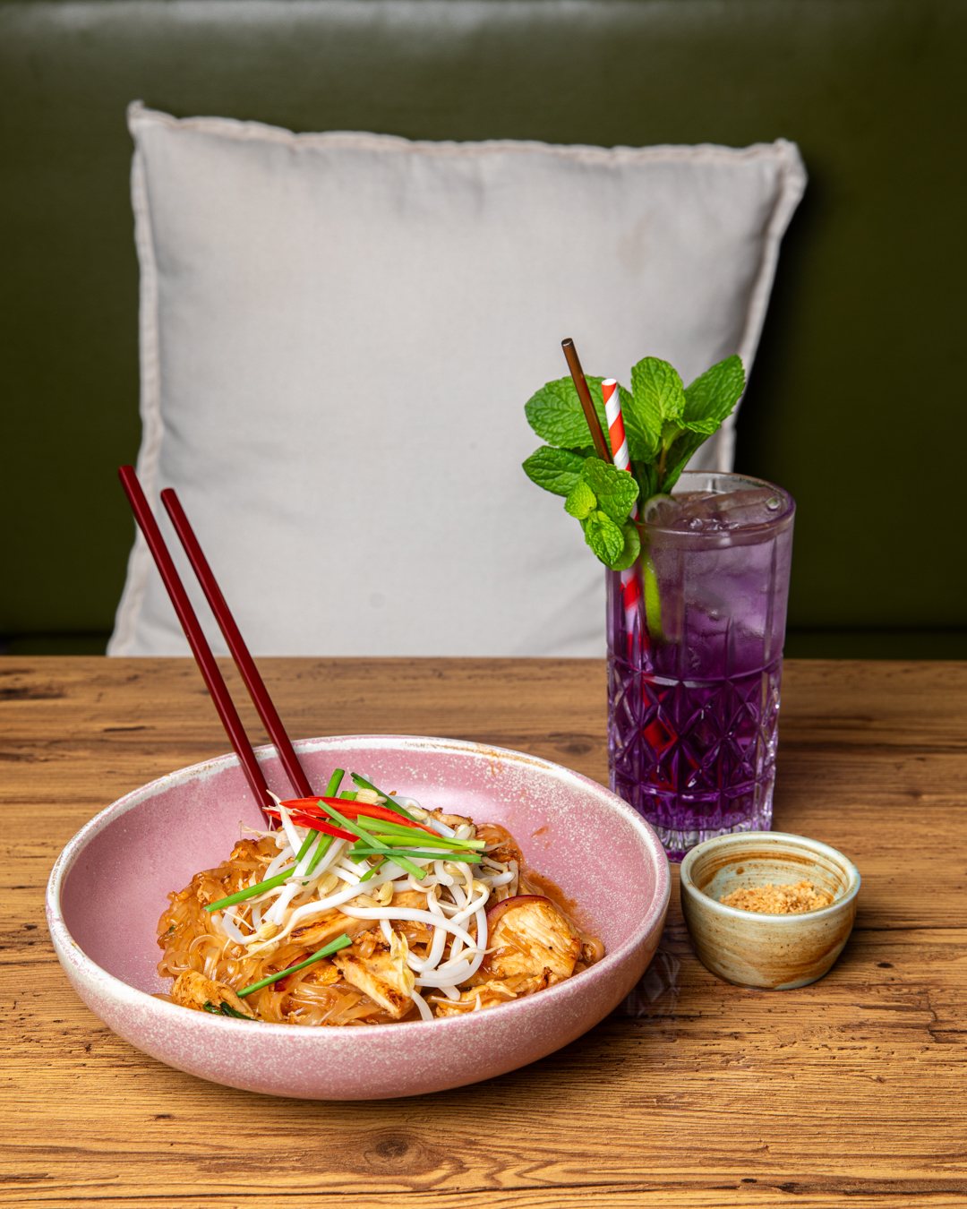 Pad Thai with red chopsticks and a purple butterfly pea cocktail on a timber table at D.C. Thai, Diamond Creek