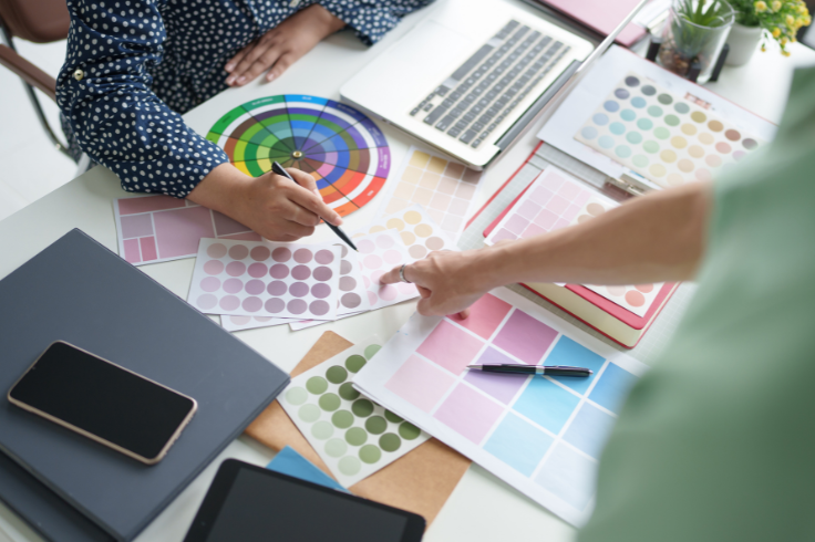 A top-down view of a design table with color swatches, a laptop, and two people collaborating on a project.