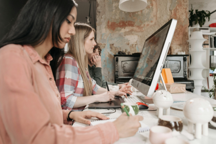Three people focused on their work at a desk with a computer and notebooks. 