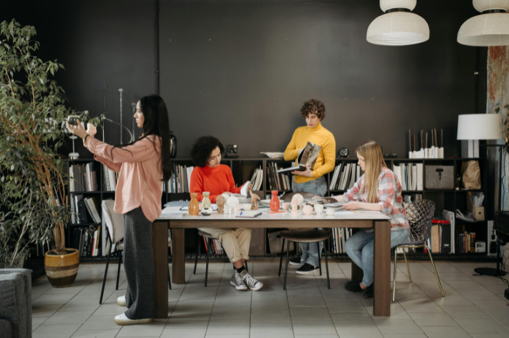 Four people are gathered around a table in a room with bookshelves. 