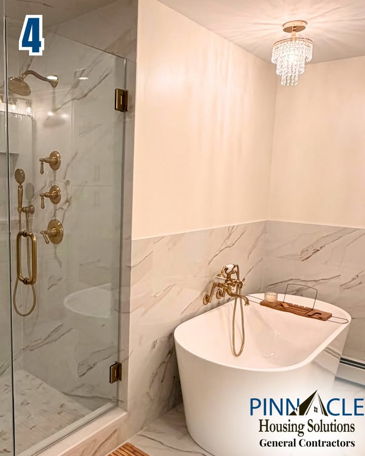 Soaking tub with a brass filler and a glass-enclosed marble-look tile shower under a crystal light in a Chester County, PA bathroom remodel.