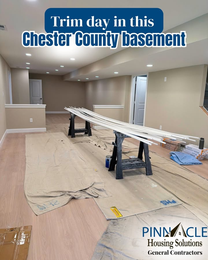 Basement remodel in Chester County, PA during trim day, with half walls, wood-look flooring, and trim pieces laid out on sawhorses.