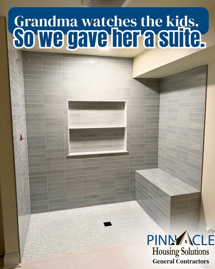 Basement bathroom remodel with a curbless walk-in shower, gray tile walls, a recessed shelf niche, a tiled bench and a pebble-style tile floor.