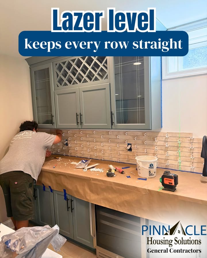 Backsplash tile going up row by row at a Chester County, PA basement bar, with a laser level sitting on the paper-covered counter.