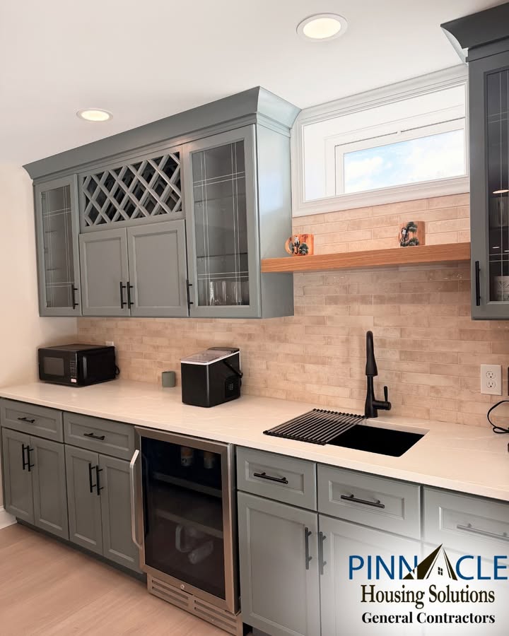 Basement bar remodel in Chester County, PA with a built-in wine fridge, floating wood shelf, tile backsplash, and black sink faucet.