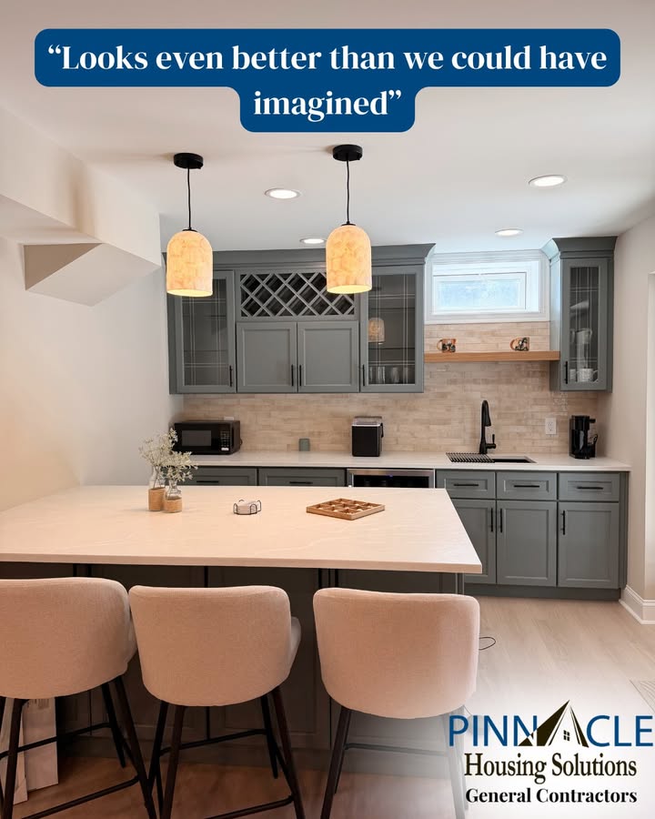 Finished basement bar with gray-green cabinets, pendant lights and a peninsula with three barstools in Chester County, PA.