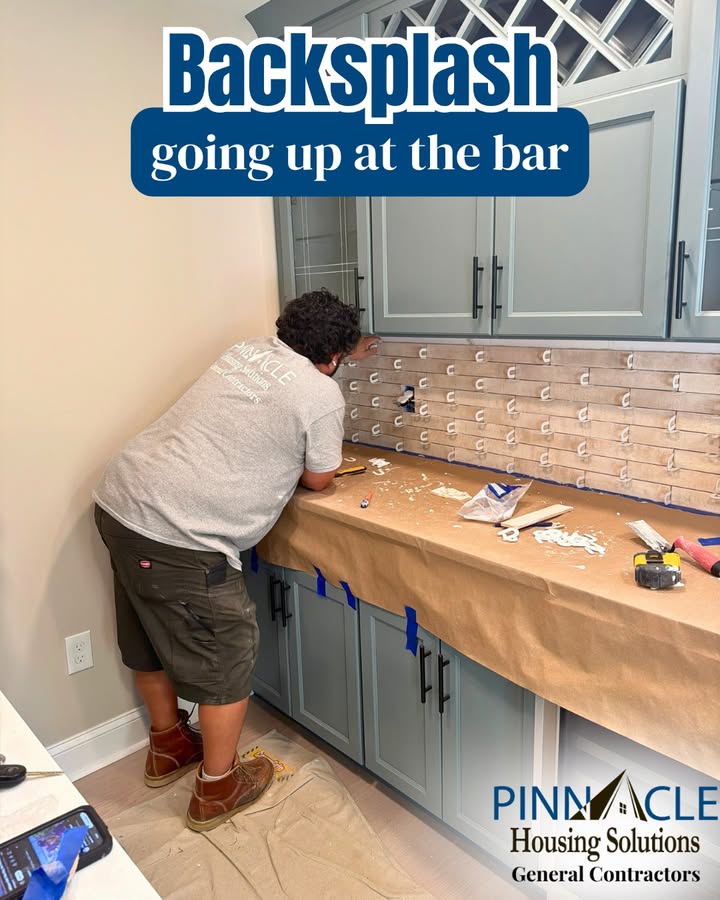 Crew member setting tile backsplash at a basement bar in Chester County, PA, with the countertop covered in paper.