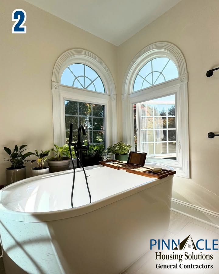 Oval soaking tub with a black floor-mounted faucet and a wood tray below two arched windows in a Chester County, PA bathroom remodel.