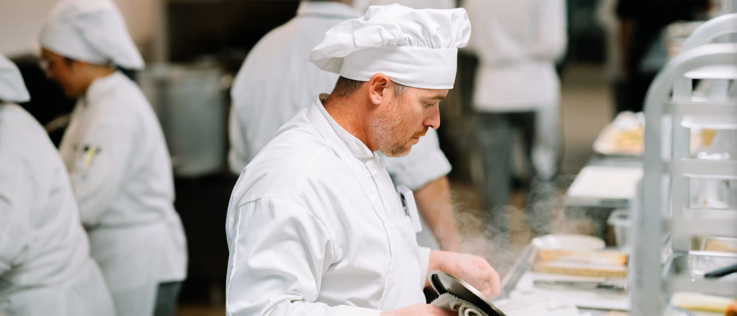 Culinary student preparing a dish during evening kitchen training