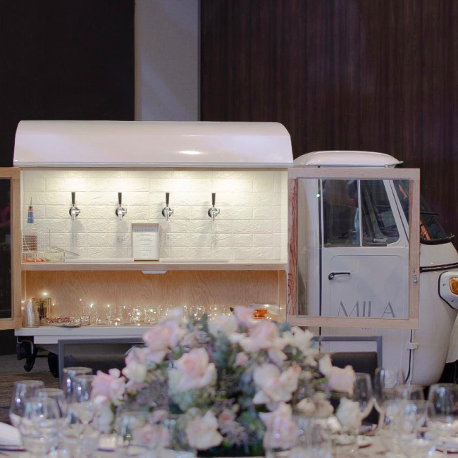 Mila Bar surrounded by floral arrangements at an event