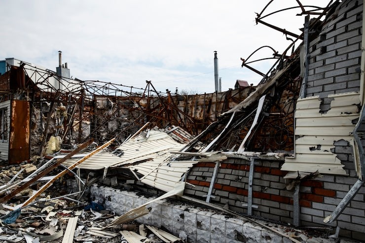 A collapsed building reveals charred beams, exposed insulation, brickwork, and scattered debris under a cloudy sky.