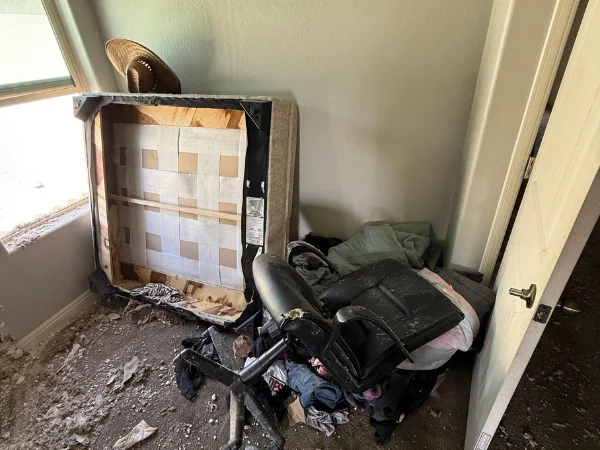 A neglected room with a damaged armchair, office chair, and debris on the floor, suggesting disrepair.