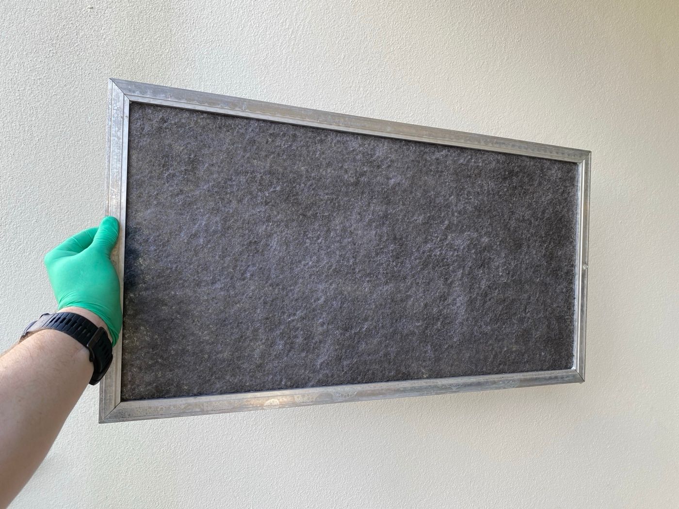 Gloved hand holding up a ducted return air filter caked in grey dust