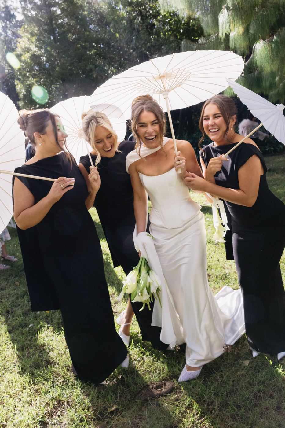 Bride laughing with her bridesmaids under paper parasols