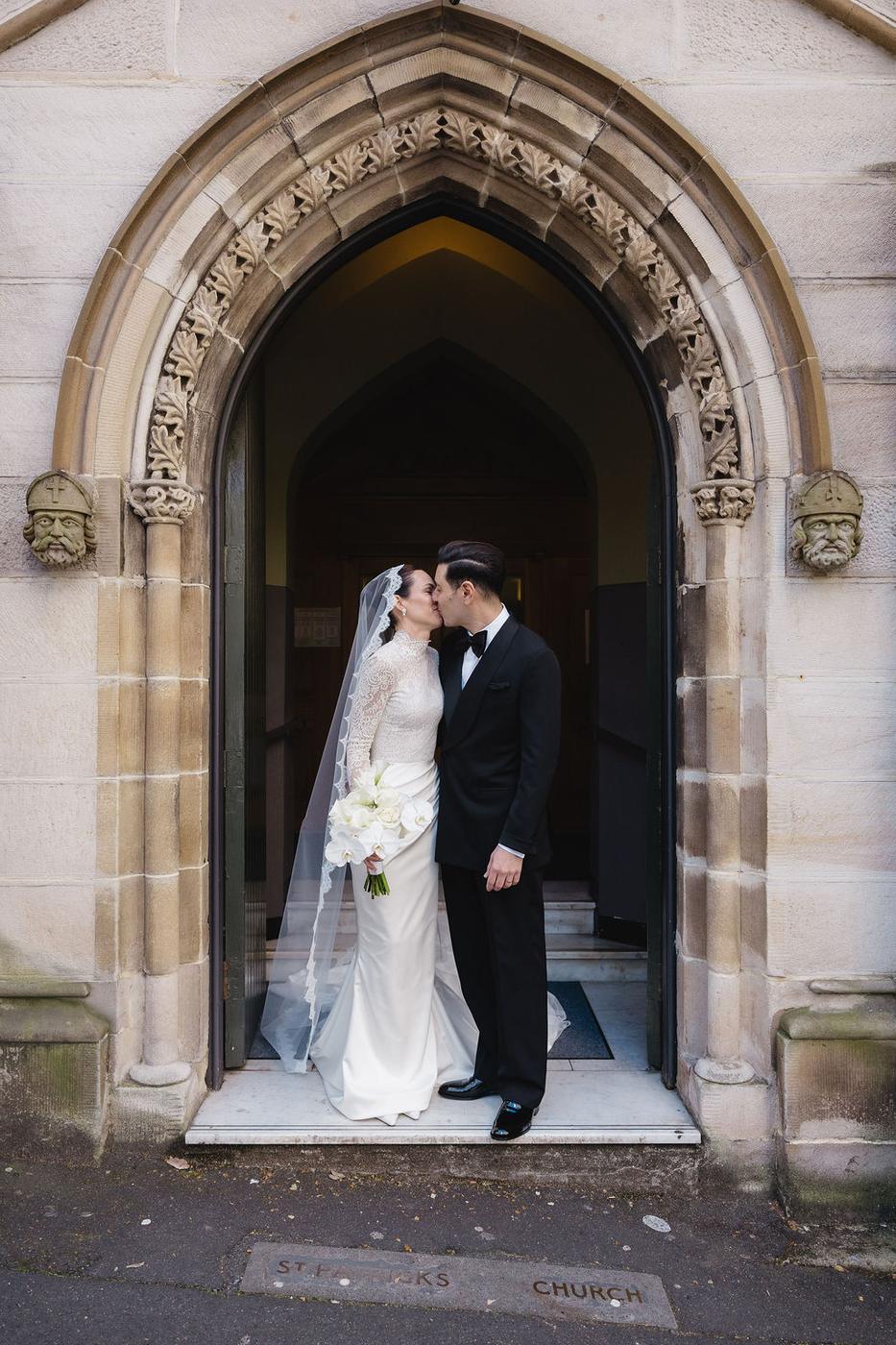 Newlyweds kissing in a carved sandstone church doorway