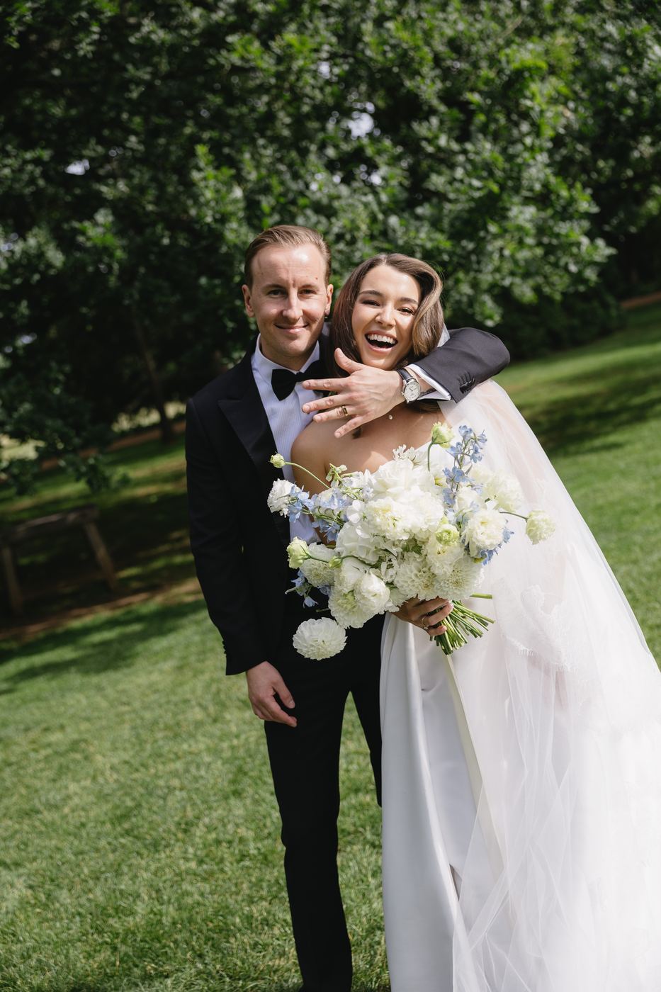 Bride hugging her groom and laughing, bouquet in hand
