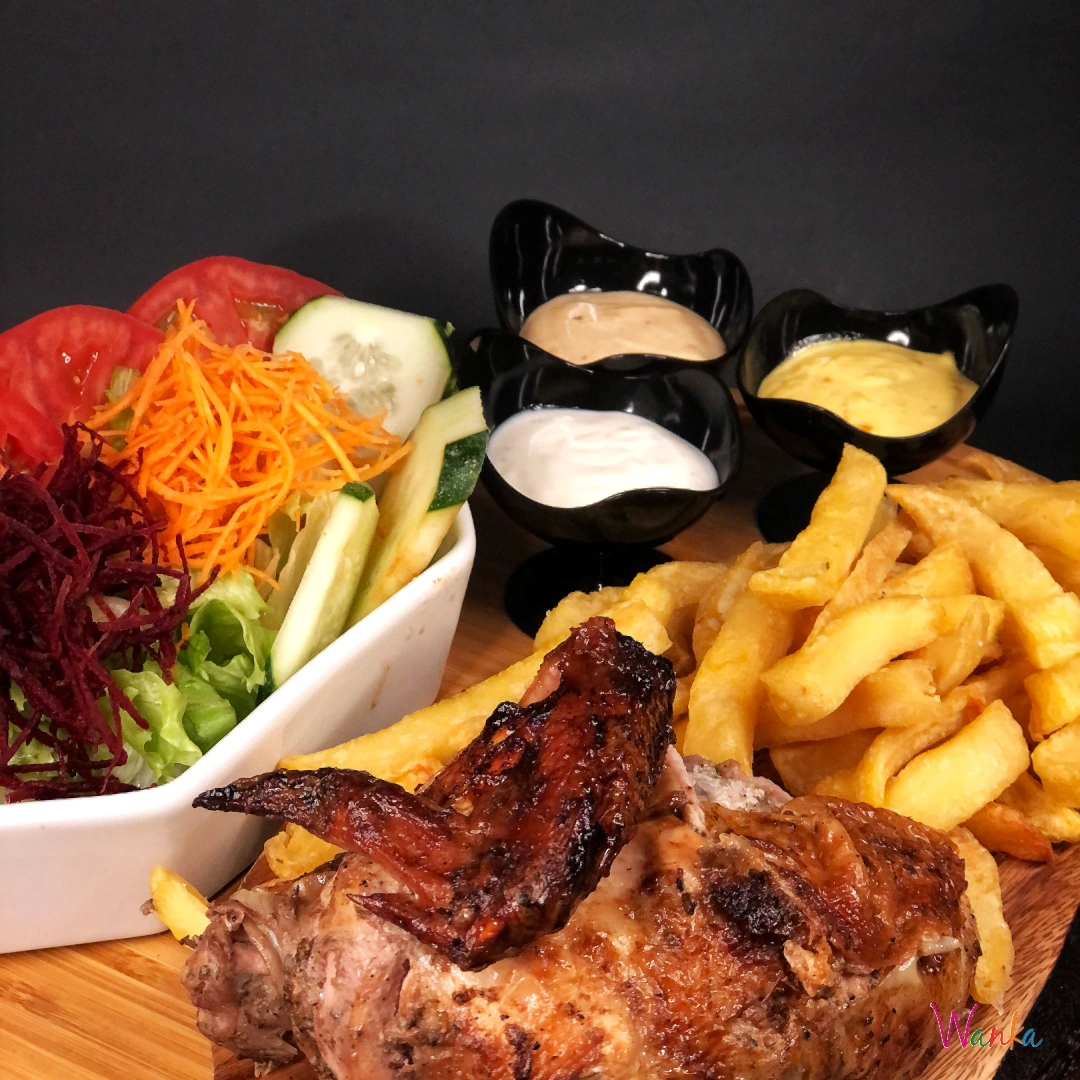 Medio pollo a la brasa con ensalada, patatas y tres salsas sobre fondo oscuro