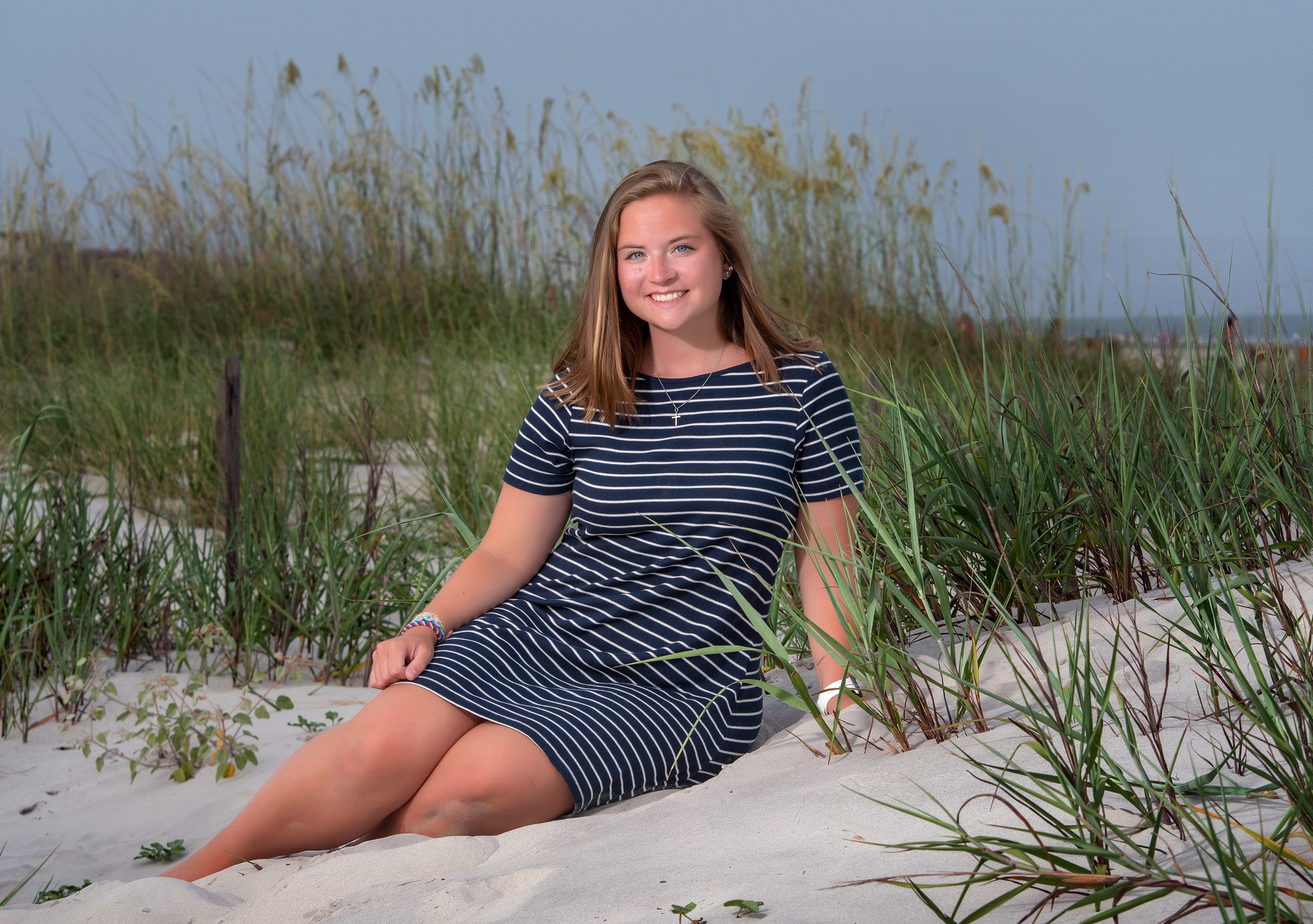 Hilton Head senior portrait of teenage girl sitting in beach dunes wearing a striped navy dress in Sea Pines.
