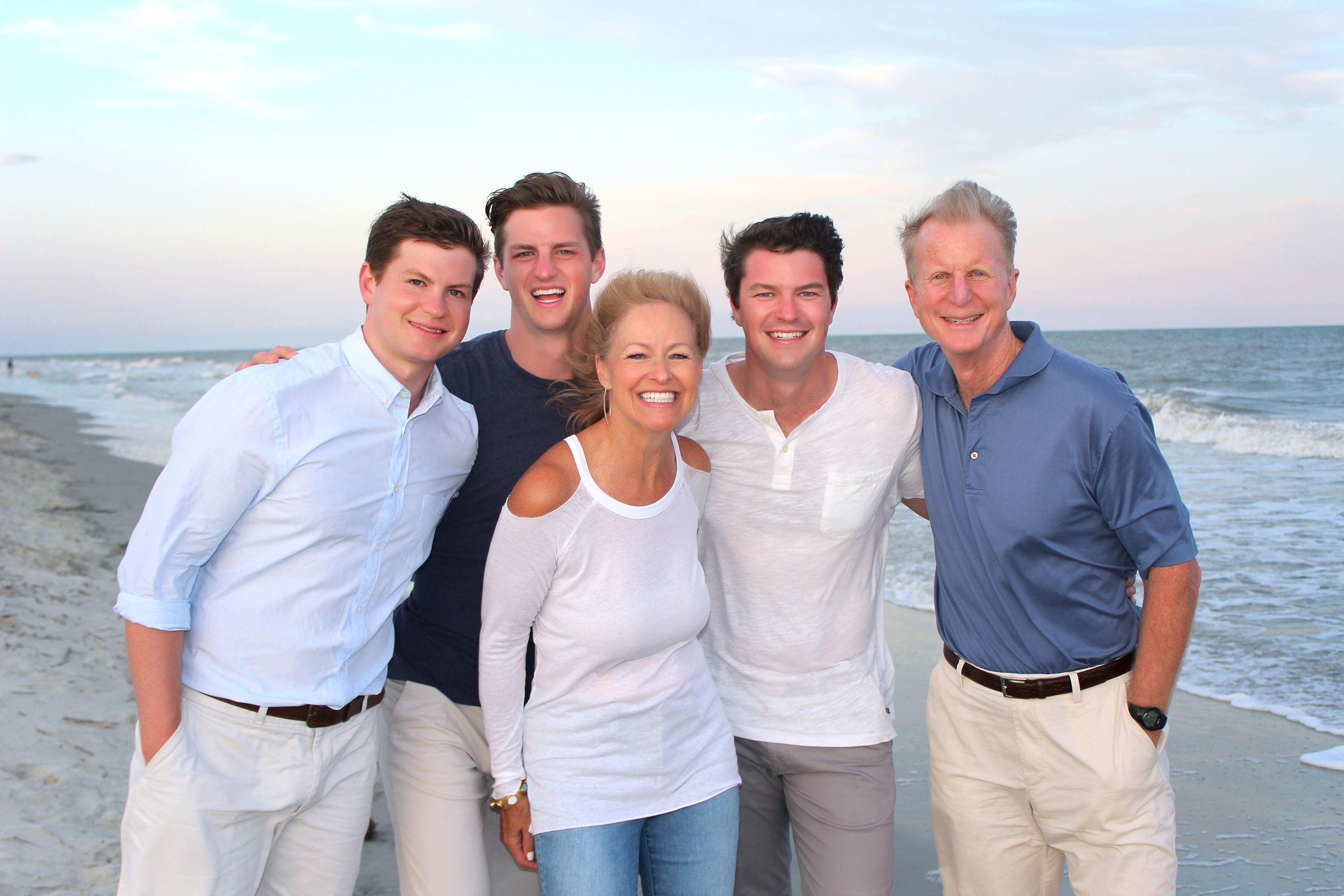 Parents with their three adult sons smiling during a beach photo session on Hilton Head Island at sunset