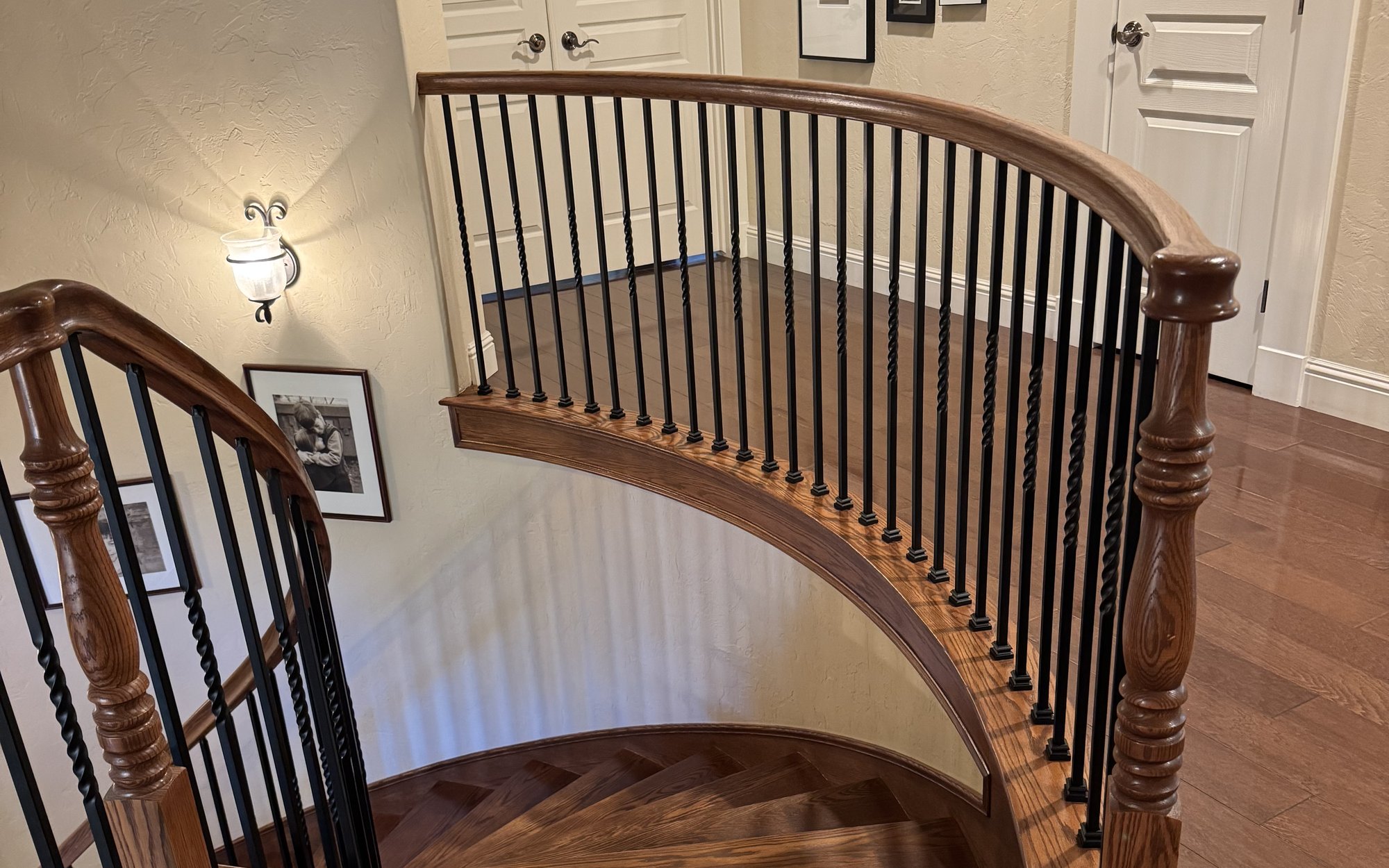 Sweeping curved staircase with a rich stained wood handrail and new black wrought-iron balusters — Alamo Stairs, Roseville, Northern California