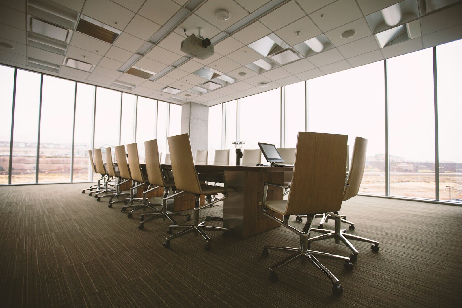 An empty conference room with a long table and office chairs by tall windows