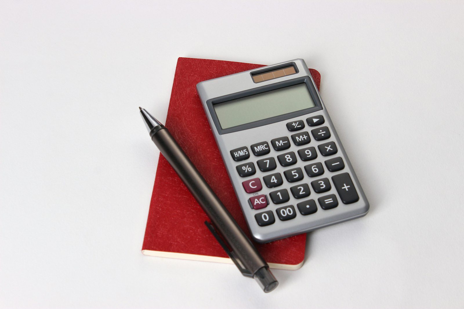 A calculator and a pen resting on a red notebook